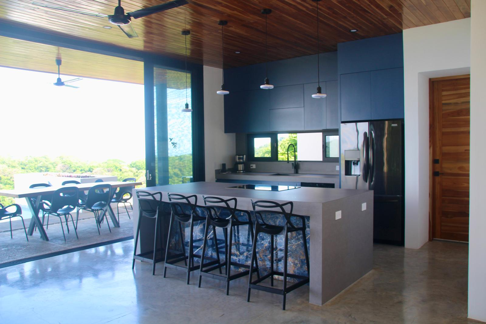 Casa Playa Carrillo — kitchen with navy cabinetry, stone island and pendant lighting opening to the terrace
