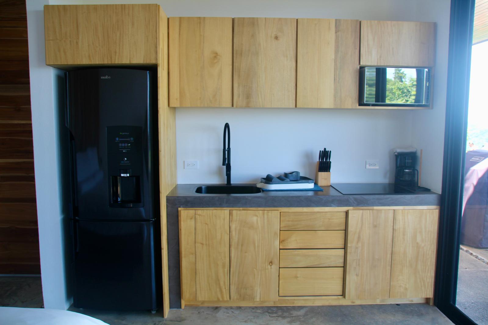 Casa Playa Carrillo — teak kitchenette with stone counter and black appliances
