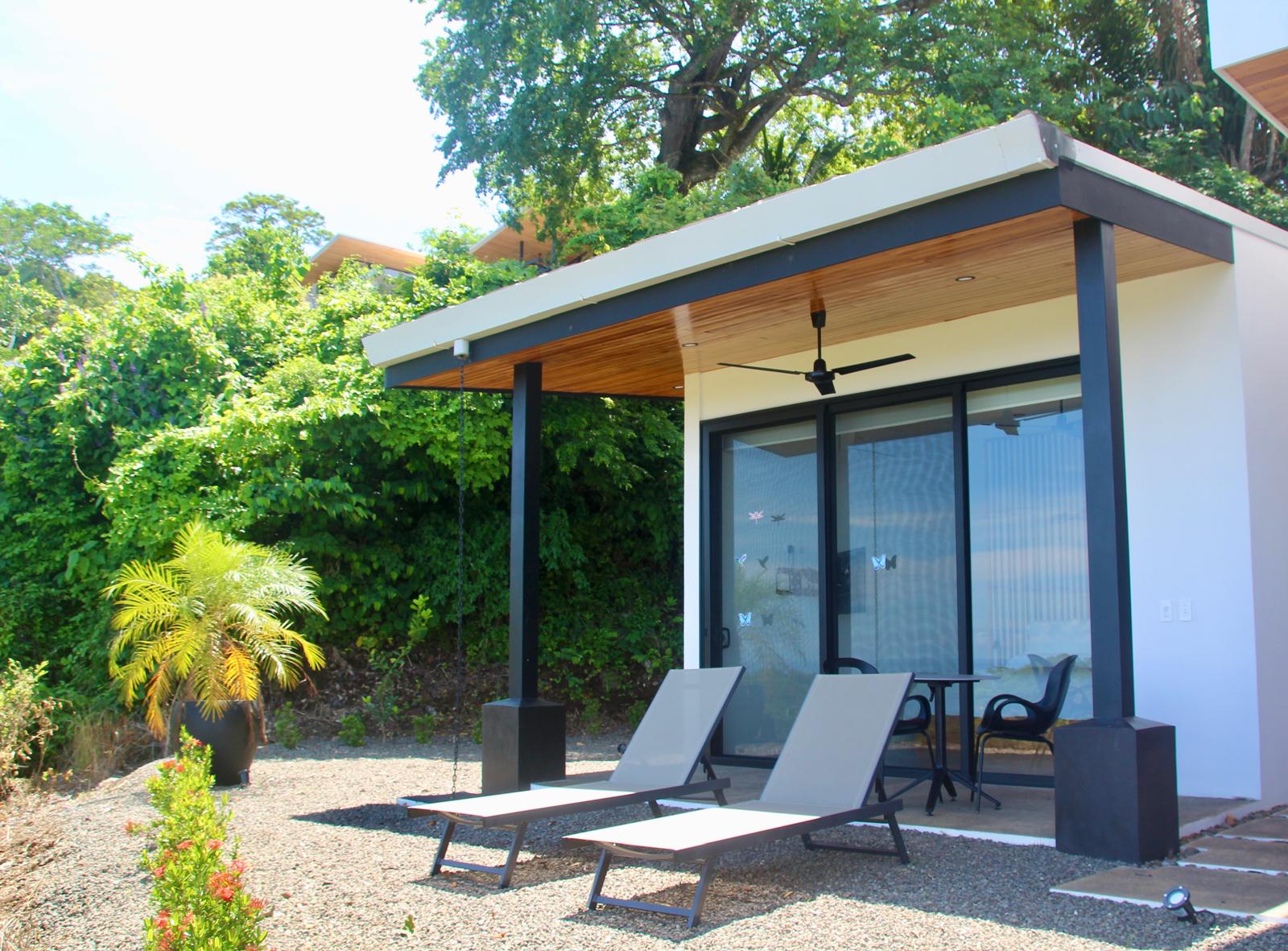 Casa Playa Carrillo — lower pavilion with sliding glass doors and sun loungers on the gravel court