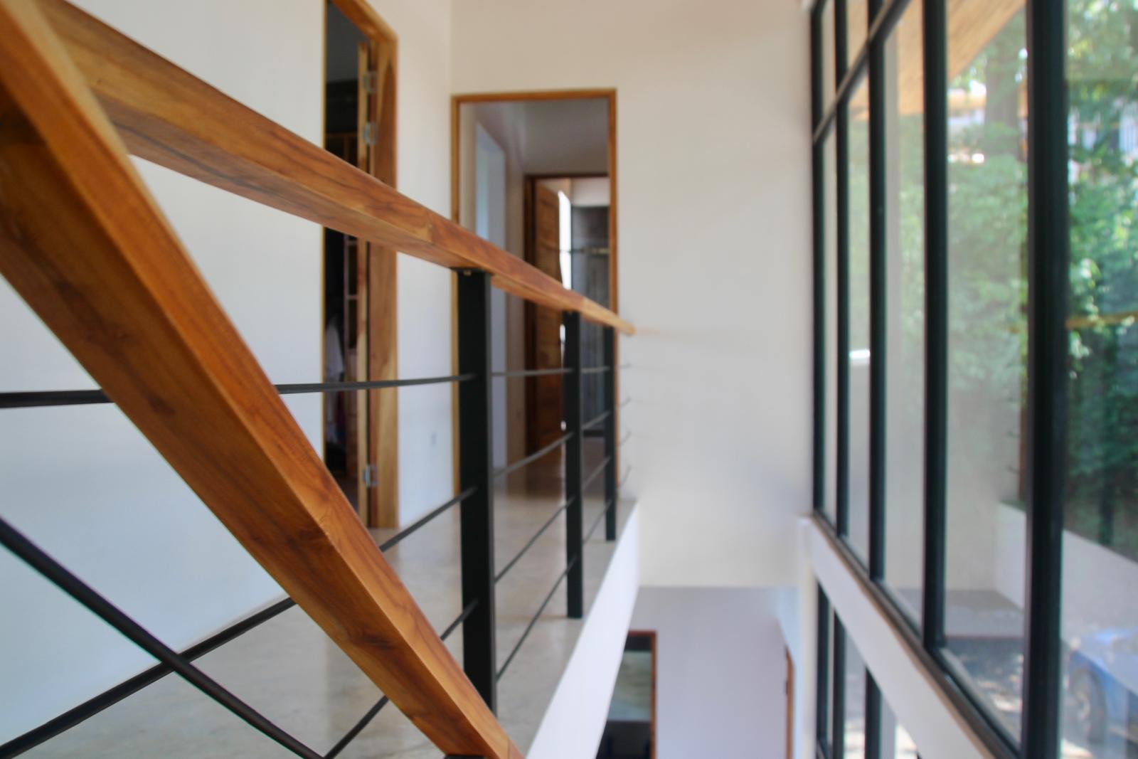 Casa Playa Carrillo — teak handrail and upper landing beside the glazed stairwell