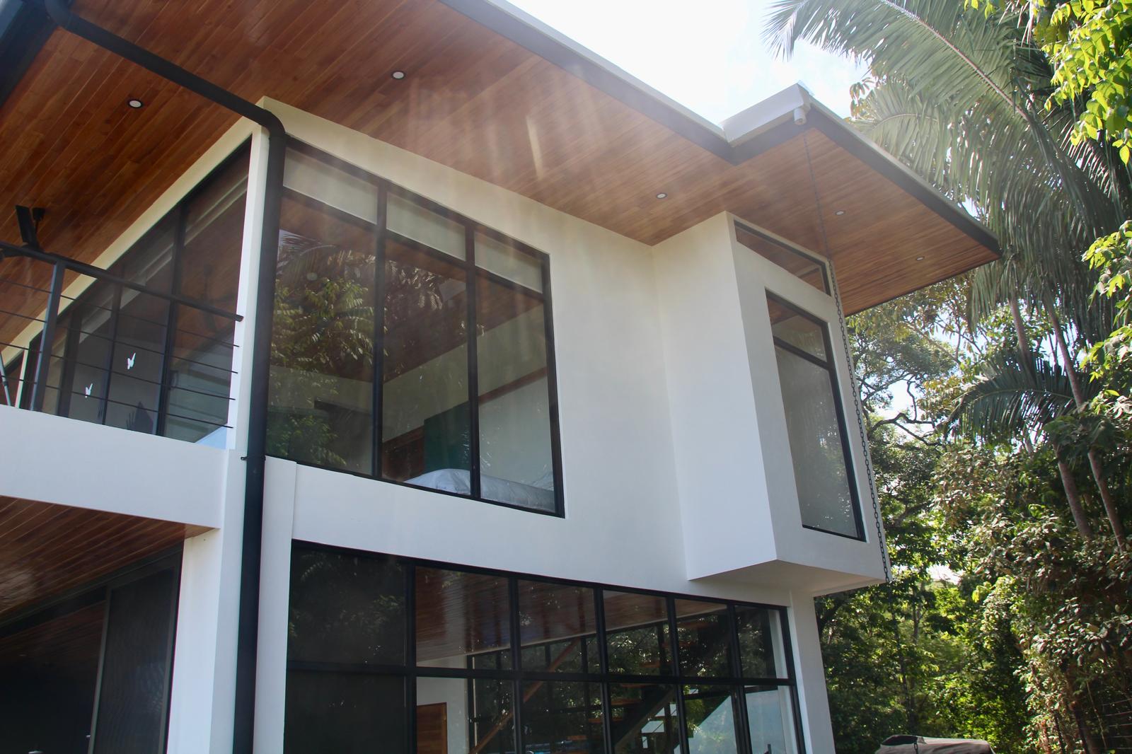 Casa Playa Carrillo — upper volume with timber soffit and black-framed windows seen from the garden