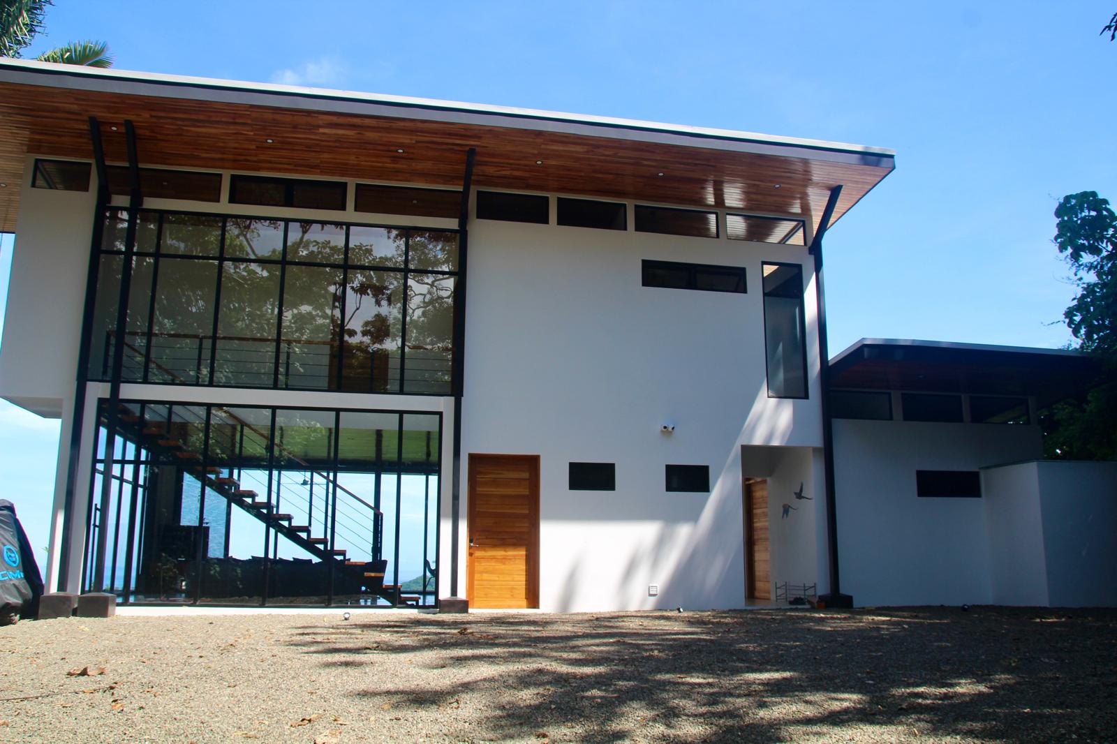 Casa Playa Carrillo — entry elevation with teak doors, tall glazing and gravel drive