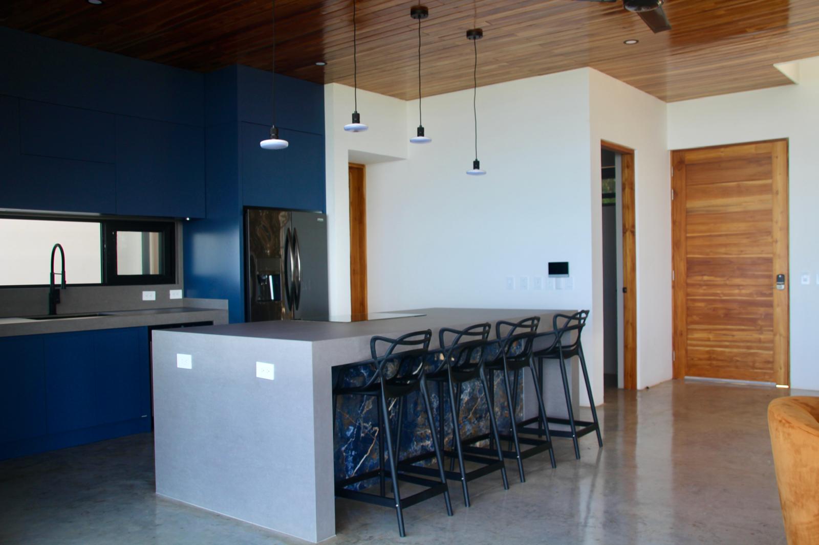 Casa Playa Carrillo — navy kitchen cabinetry, stone island and teak interior door