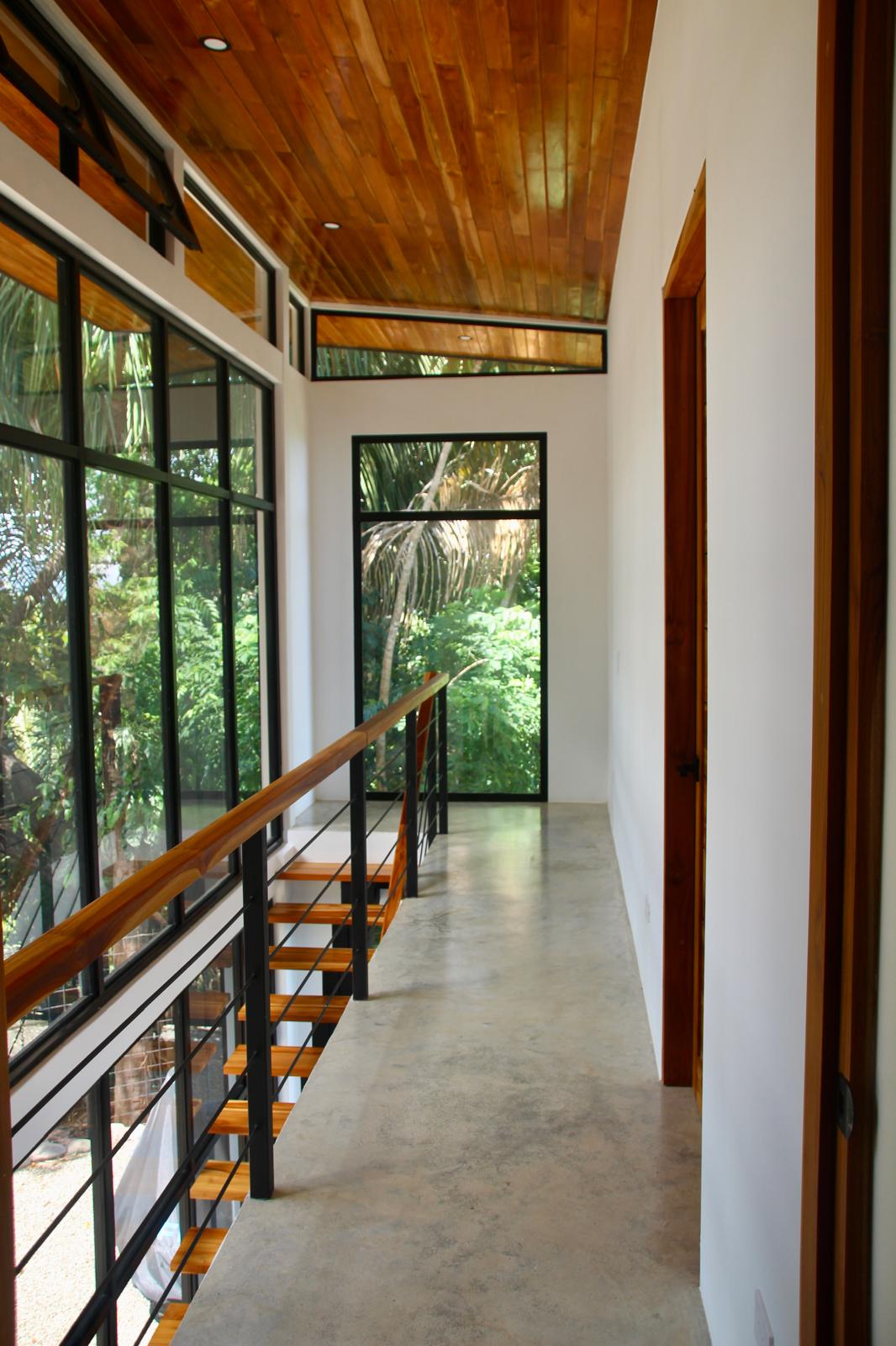 Casa Playa Carrillo — upstairs corridor beside the glazed stairwell, with teak door frames